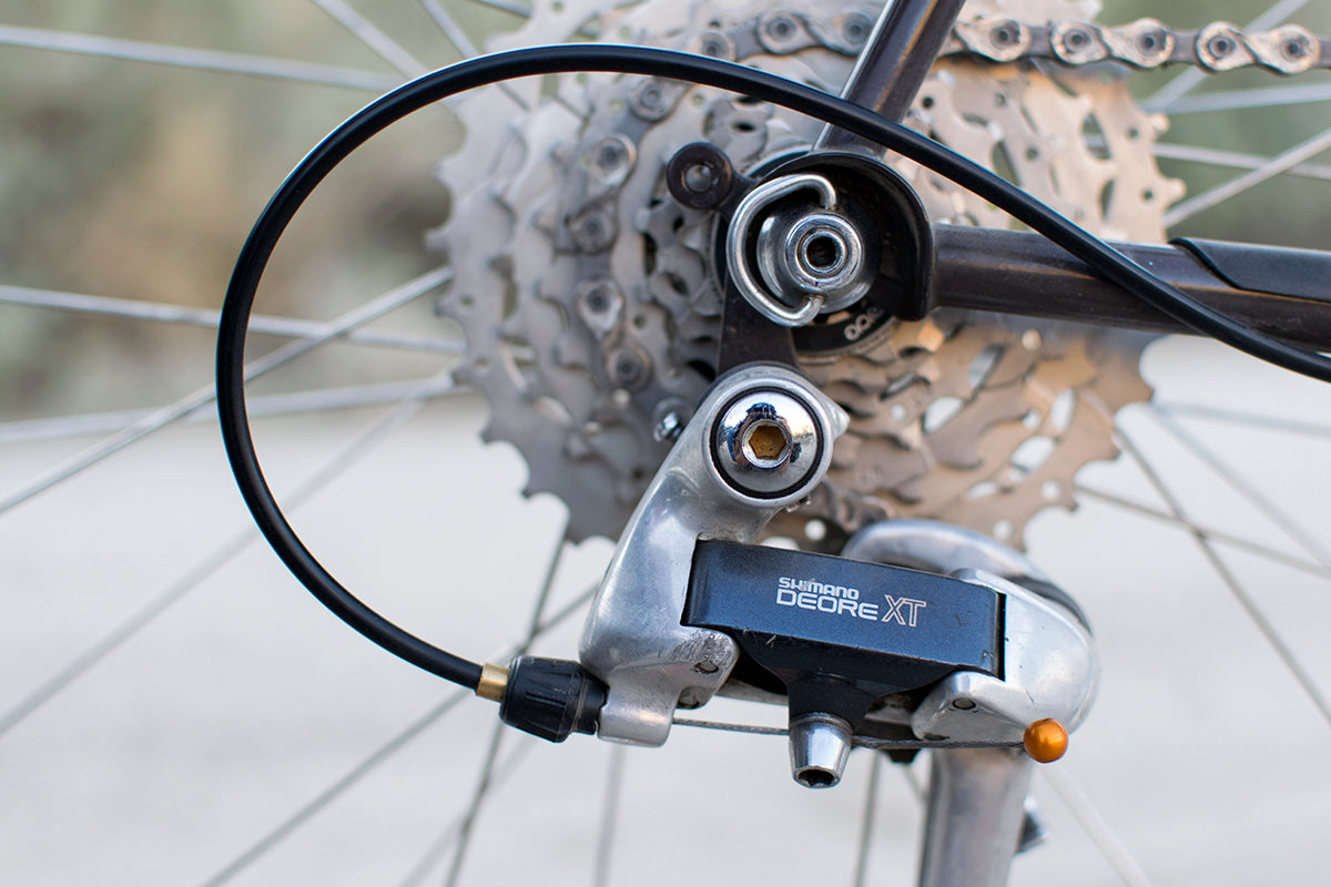 Close-up of a Shimano Deore XT bike derailleur with an orange cable cherry.