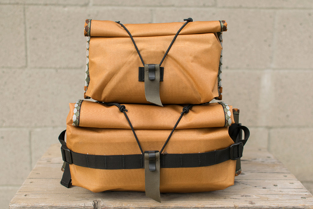 Two orange hip packs with Brown Trout patterned trim tape stacked on top of each other.
