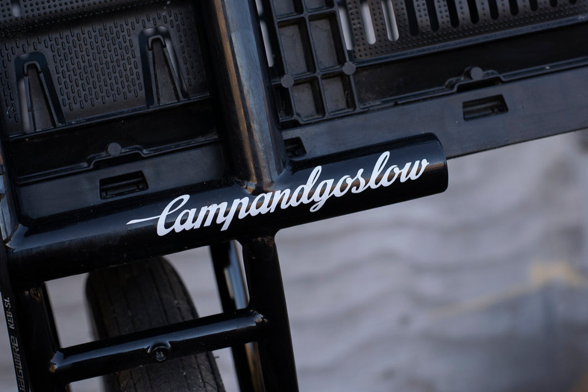 Close-up of a black bike rack with 'Camandgoslow' die-cut sticker