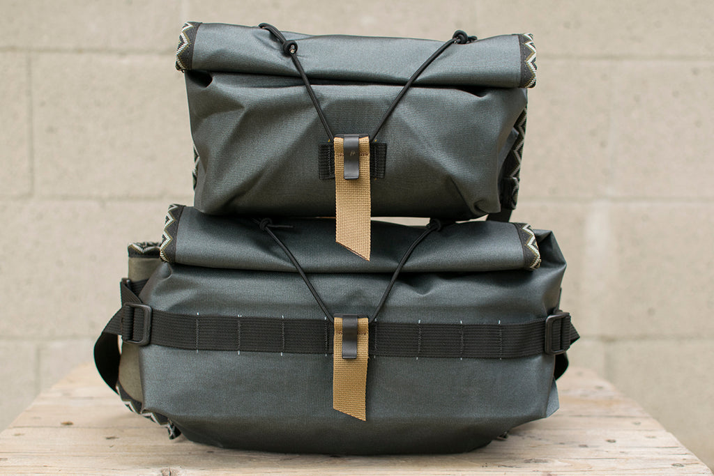 Two grey hip packs with Eastern Rattler patterned trim tape stacked on top of each other.