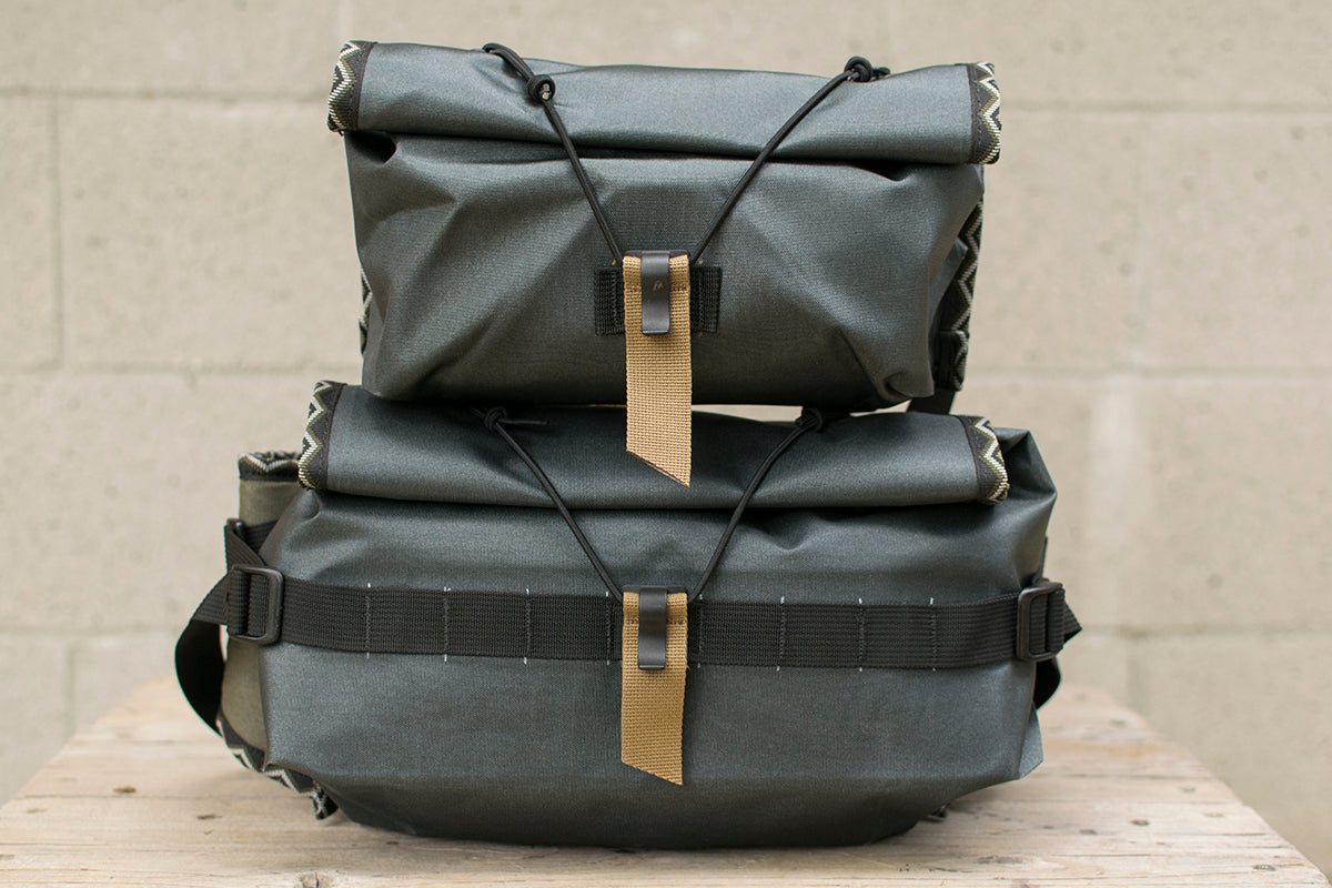 Two grey hip packs with Eastern Rattler patterned trim tape stacked on top of each other.