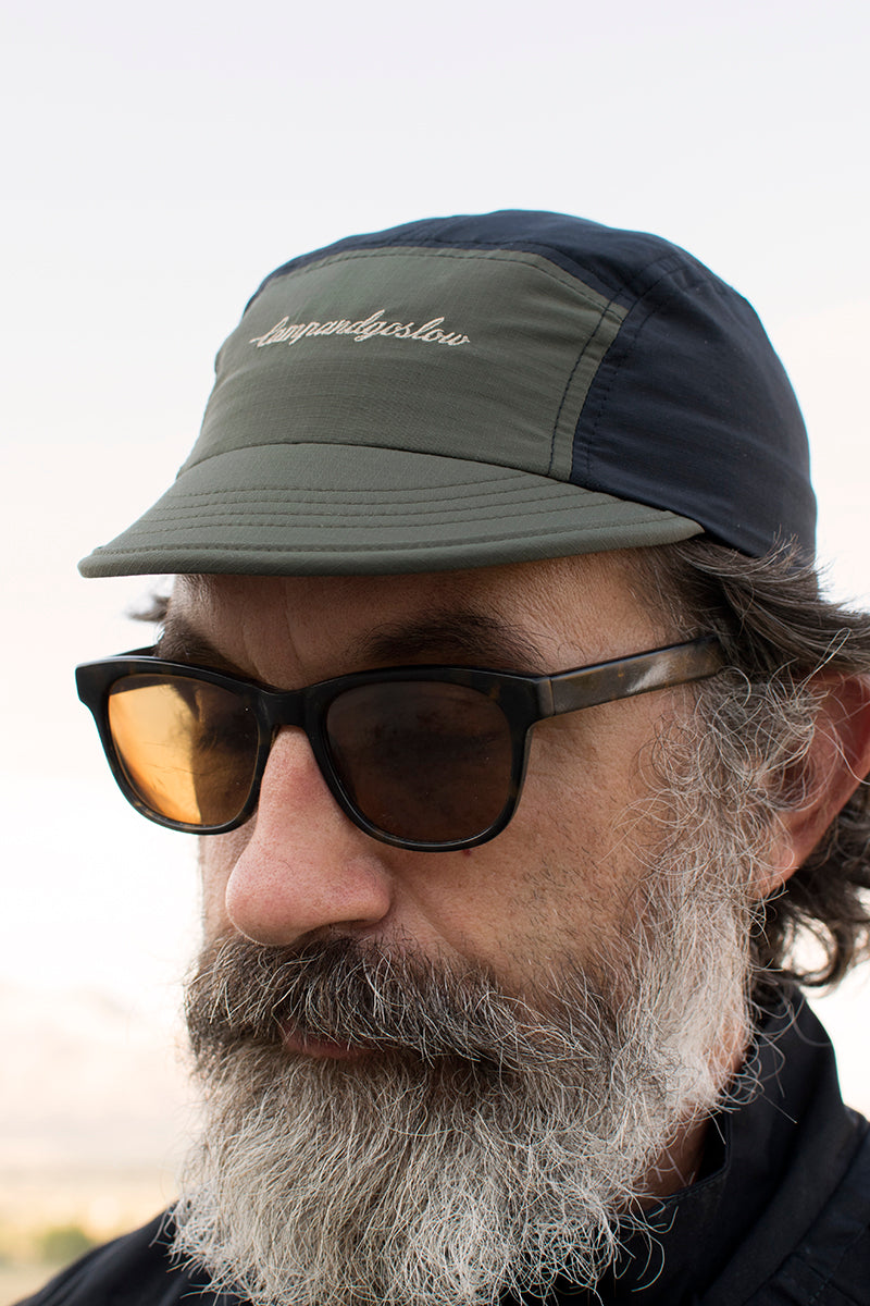 Man wearing a five panel cap and sunglasses with a blurred background