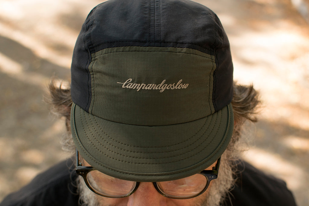 Person wearing a five panel cycling cap with Campandgoslow branding against a blurred natural background