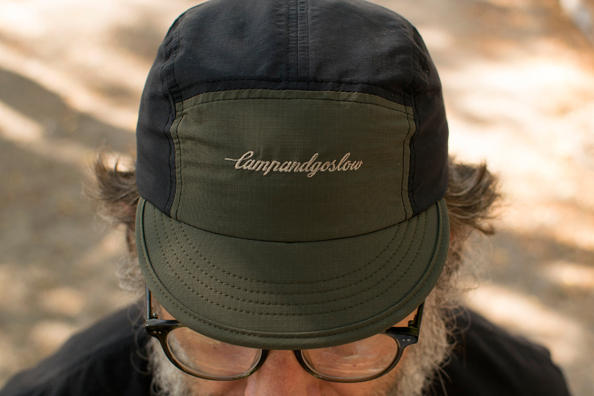 Person wearing a five panel cycling cap with Campandgoslow branding against a blurred natural background