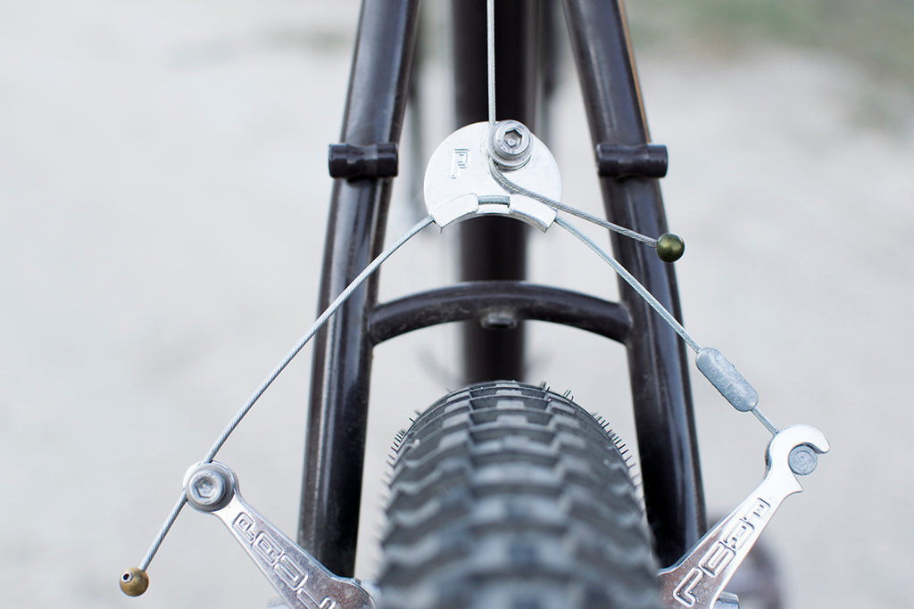 Close-up of a bicycle's suspension fork with brass and green cable cherries.