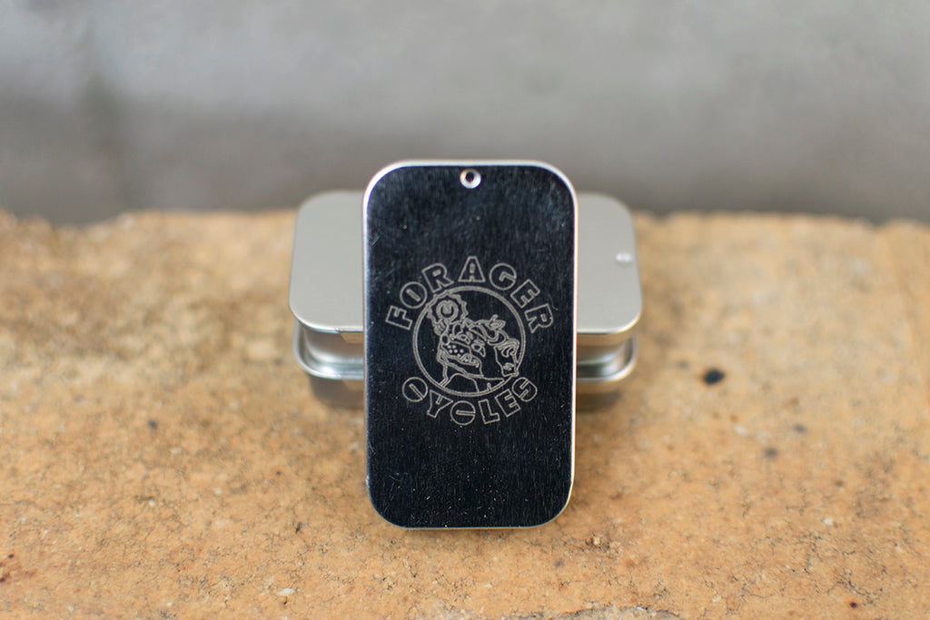 Tin with 'Forager Cycles' branding on a blurred textured background