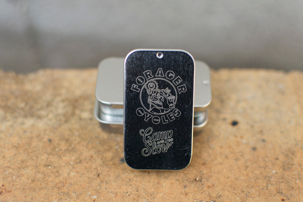 Tin with 'Forager Cycles' and 'Camp And Go Slow' branding on a textured surface