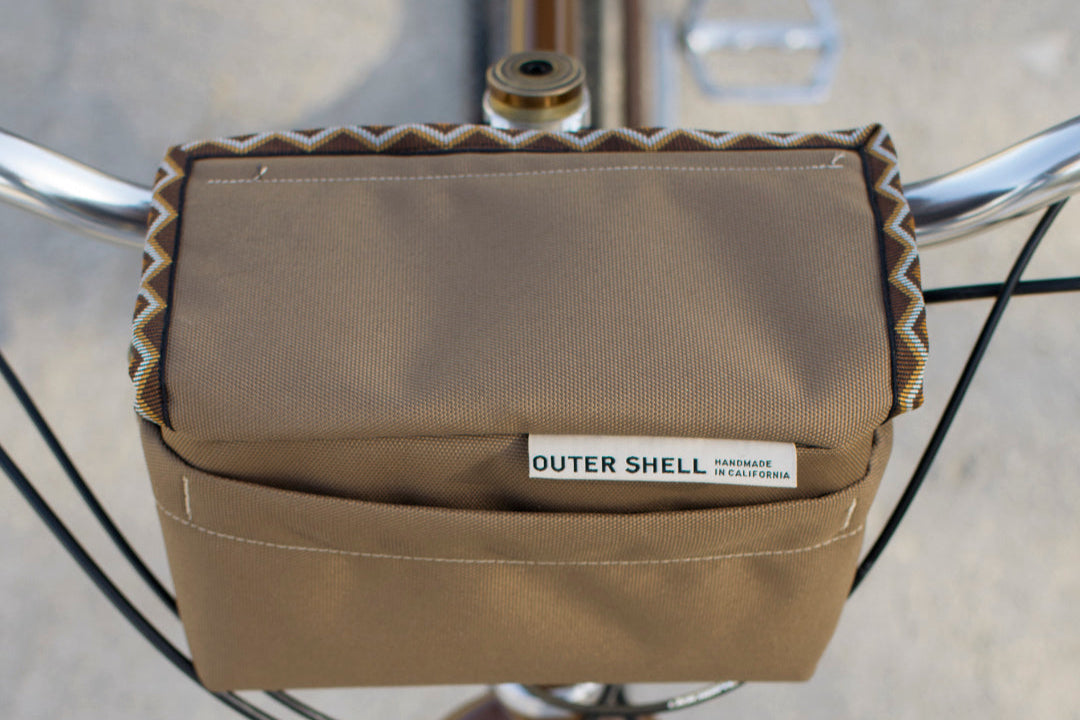 Brown Outershell bicycle bag with Western Rattler trim tape attached to a bike handlebars.