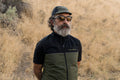 Man wearing sunglasses, a cycling cap, and a black and green vest.