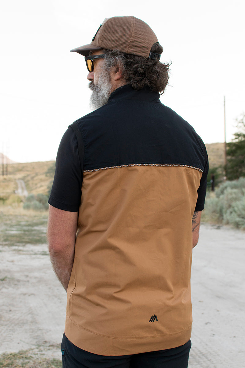 Man wearing a black and tan ventile vest and a brown hat.