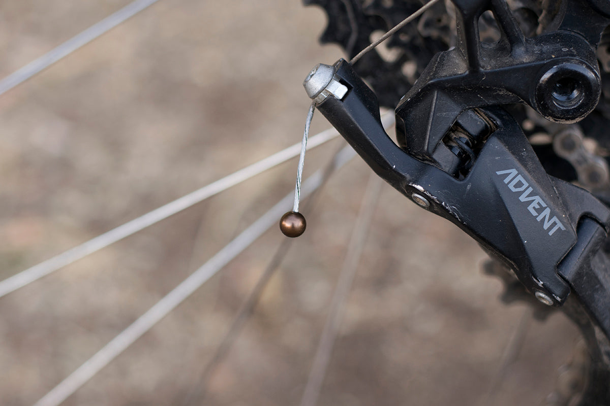 Brown cable cherry hanging from the shift cable of a microSHIFT Advent rear derailleur.