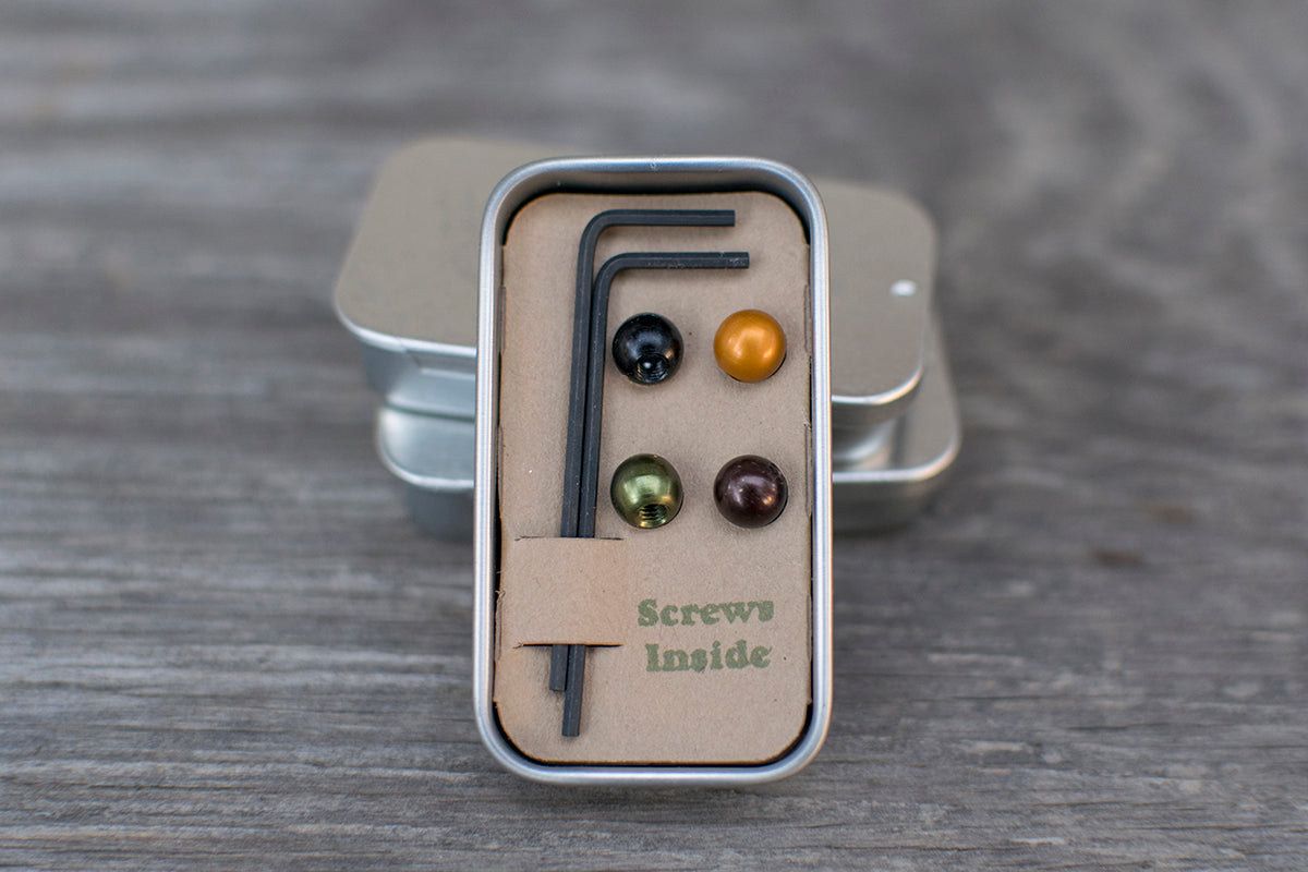 Open Forager Cycles tin holding one green, one brown, one black and one orange cable cherry with hex keys.